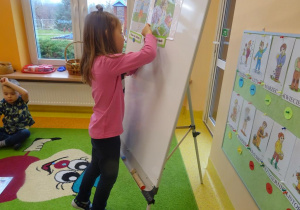 Dziewczynka przywiesza na tablicy ilustracje prezentującą jedno z praw dziecka.